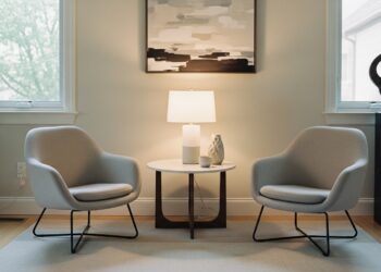 A cozy corner in a living room featuring a beige armchair with a throw blanket, a wooden side table with a mug, and a floor lamp—ideal for a secondary furniture grouping setup.