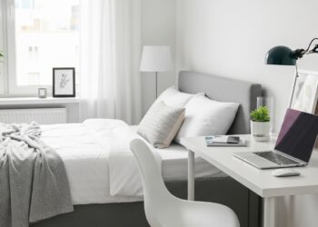 A beautifully decorated spare bedroom seamlessly blending a comfortable guest bed with a compact, well-lit home office setup, featuring warm lighting, soft textiles, and organized shelving.