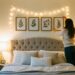 A young woman hanging botanical wall art in a cozy bedroom decorated with fairy lights and plants, representing a DIY bedroom decor idea for a tranquil space.