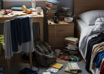 A realistic photograph of a very messy bedroom, featuring scattered clothes, books, and personal items on the floor and furniture, conveying the need for a thorough cleaning.